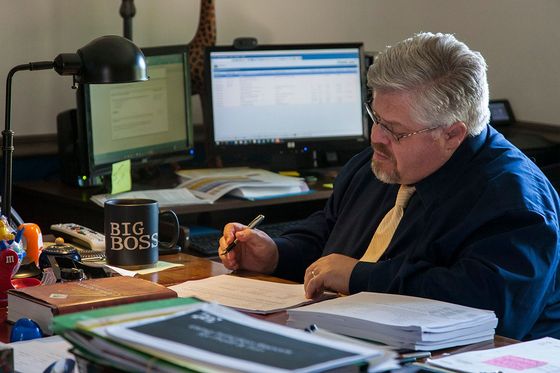 Man in a suit seated at a desk, writing on paper.