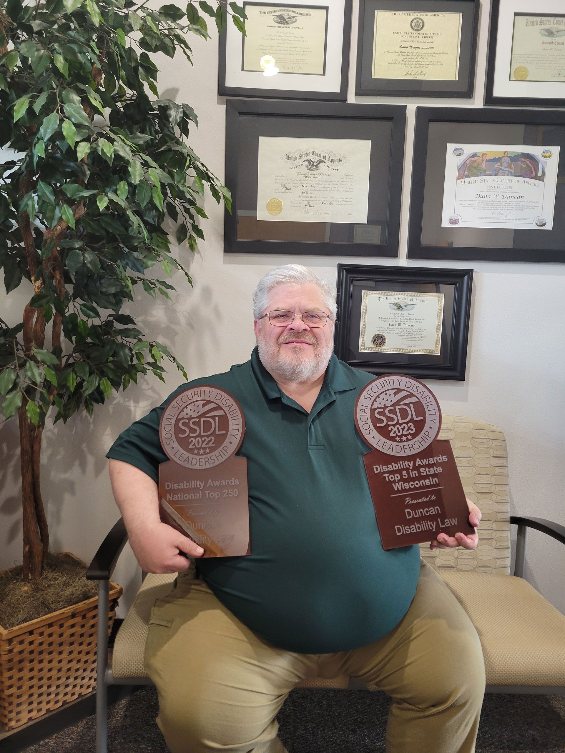 A man is sitting in a chair holding two awards