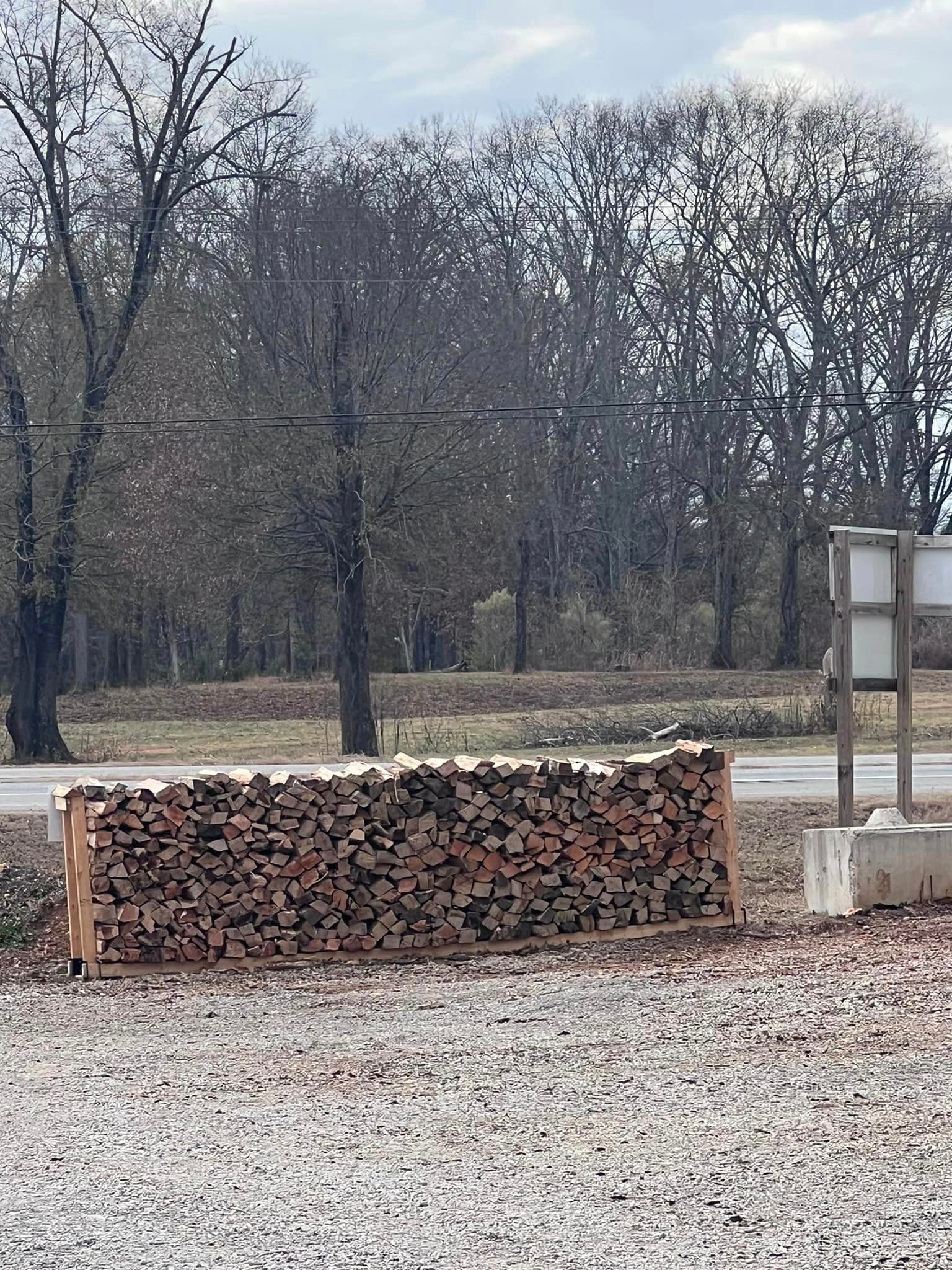 a pile of logs is sitting in a gravel lot next to a road