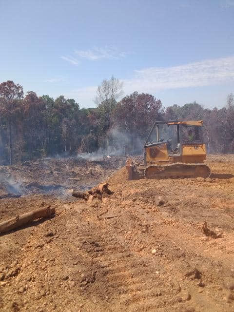 a bulldozer is moving dirt in a field with trees in the background