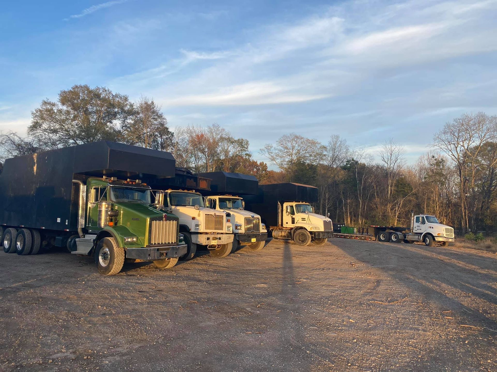 a row of semi trucks are parked in a gravel lot