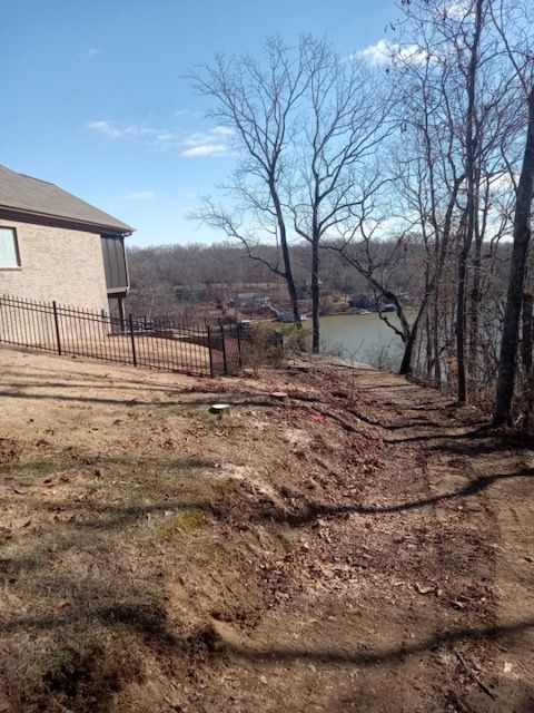 a house is sitting on top of a hill next to a lake