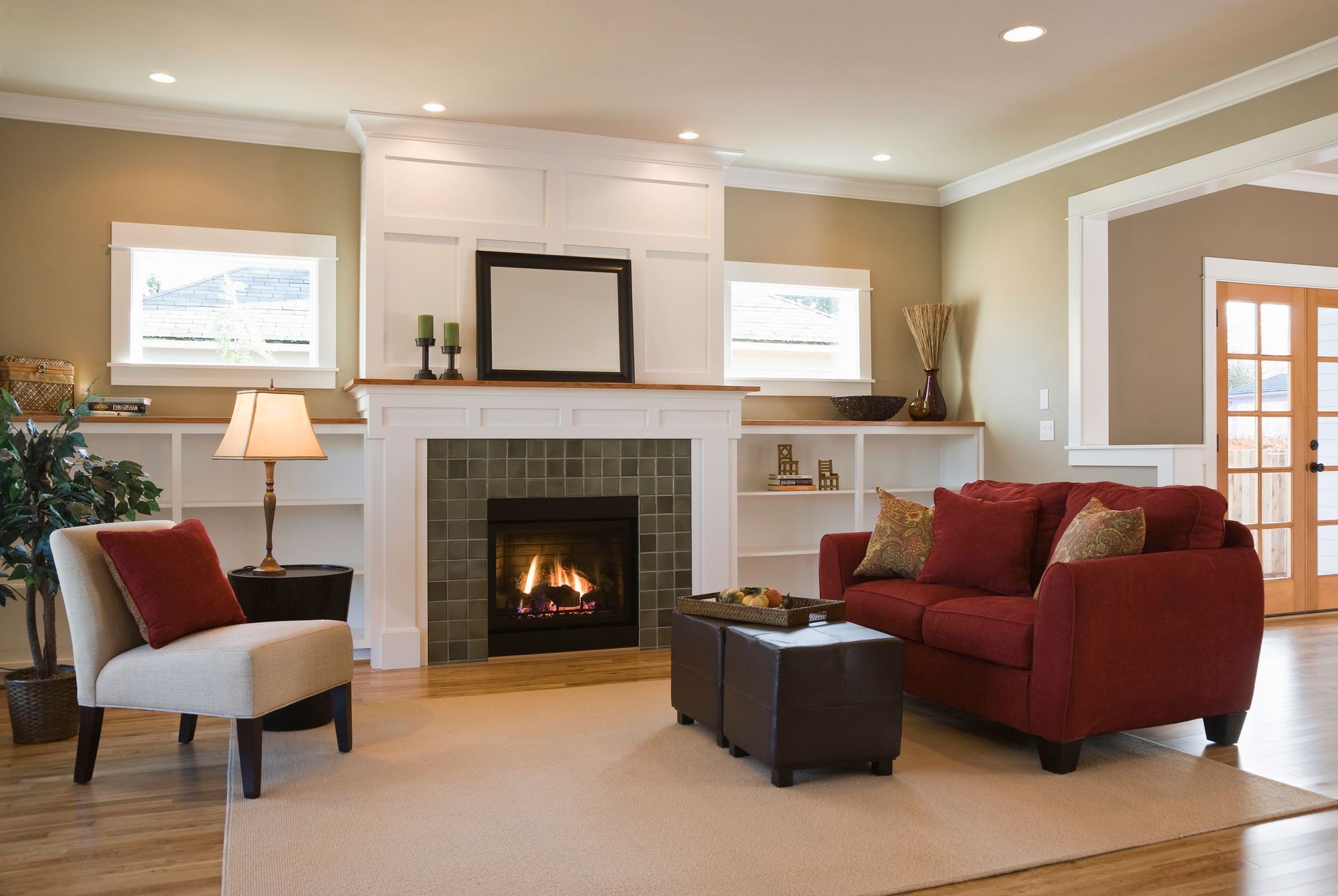 Cozy living room with fireplace, red couch, cream chair, neutral walls, and wood flooring.