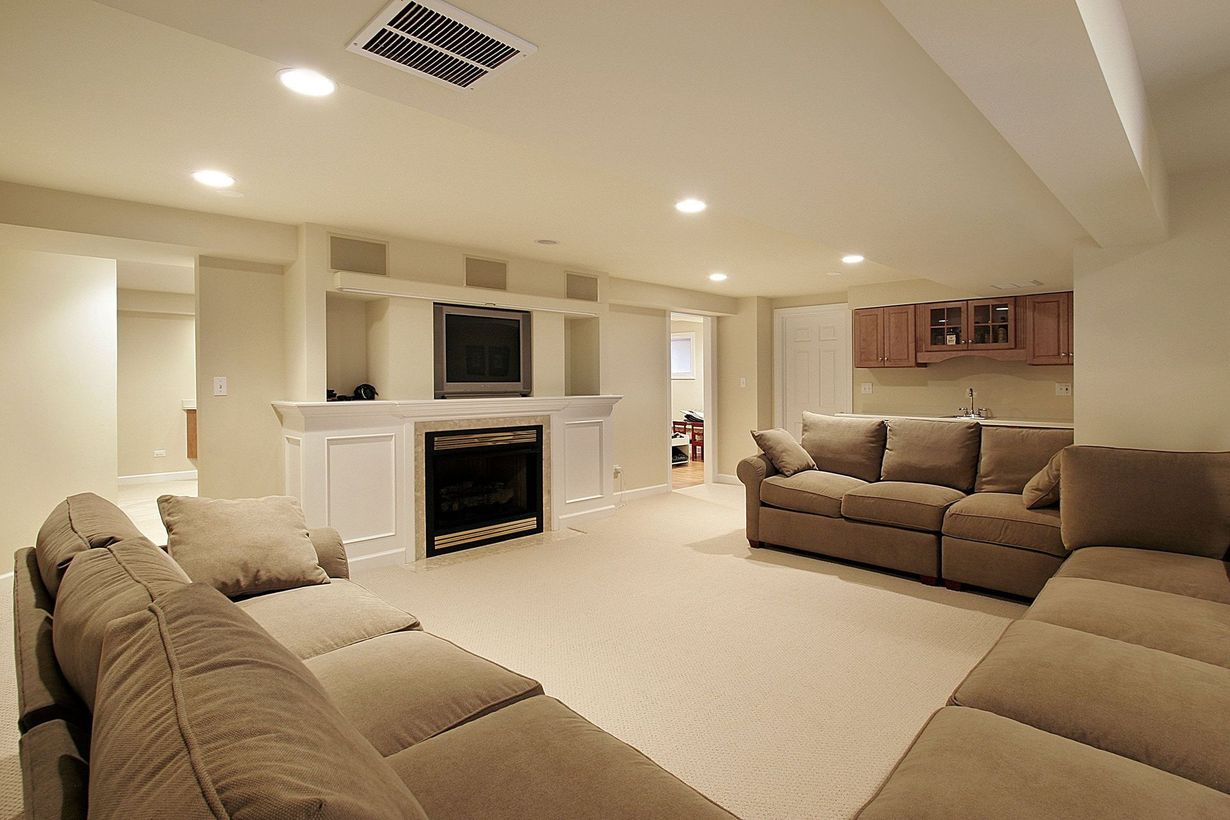 Cozy finished basement with beige sectional sofa, fireplace, and TV, warm lighting.