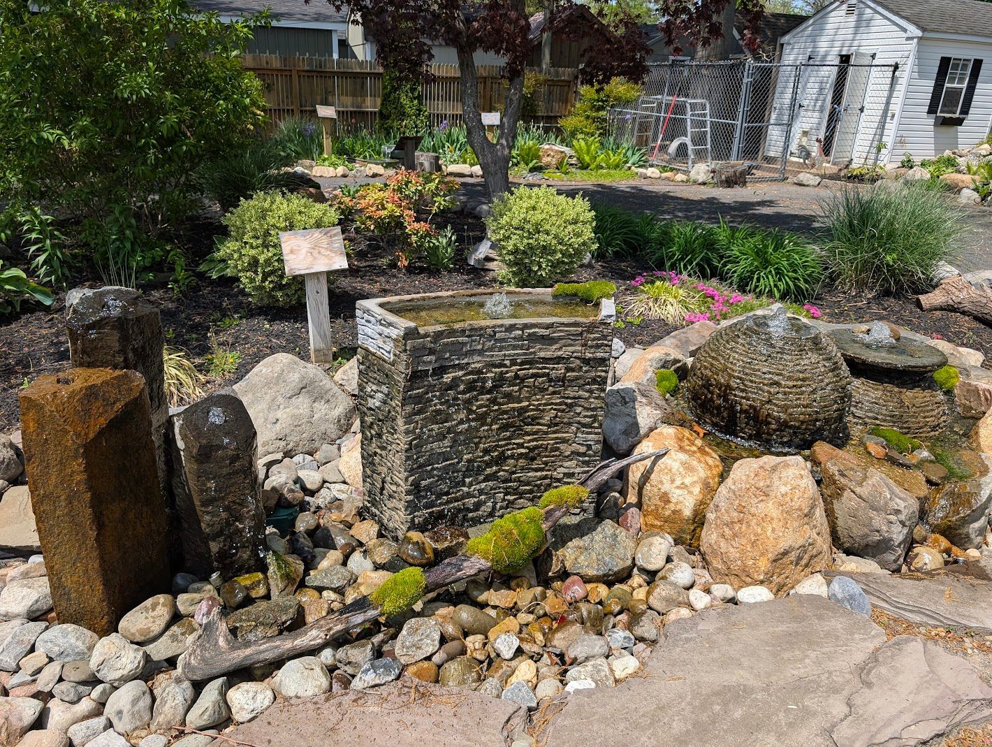 A stone fountain surrounded by rocks and greenery in a garden setting.