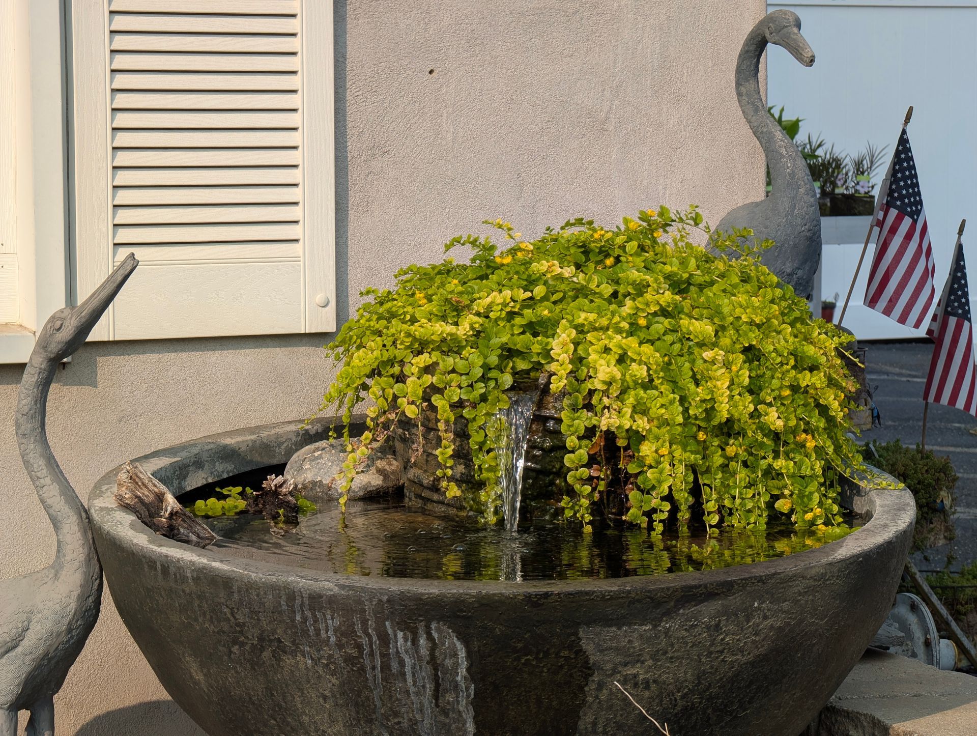Water fountain with cascading green plant, gray swan statues, and American flags.