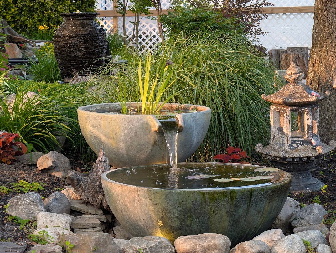 Water fountain in a garden with stone bowls and greenery.
