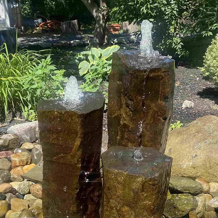 Water fountain with three stone pillars in a garden setting.
