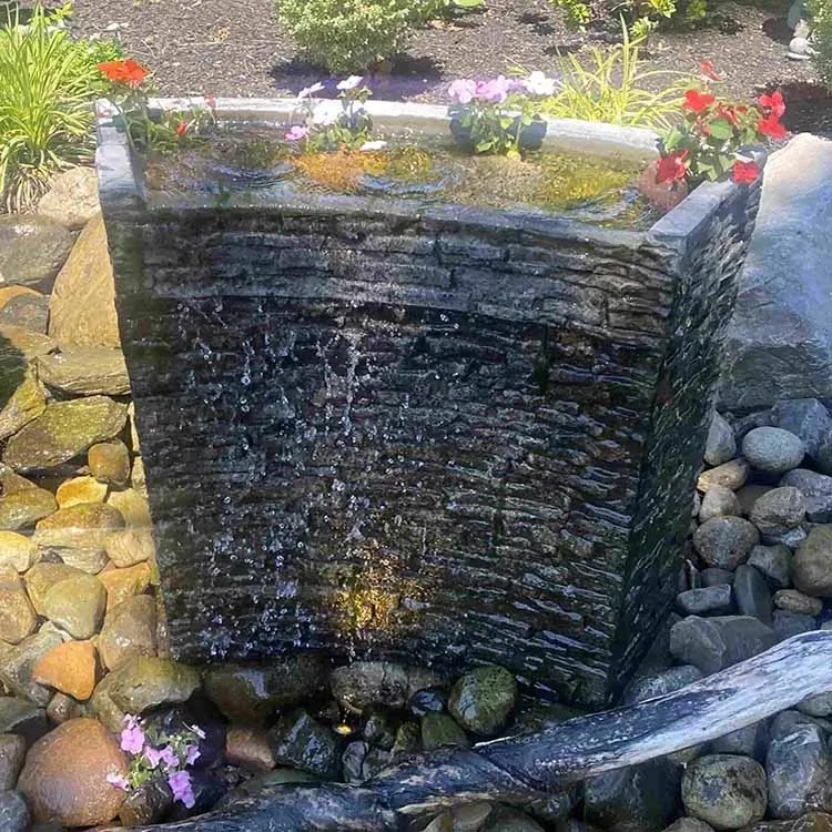 Stone fountain with cascading water and flowers in a garden setting.
