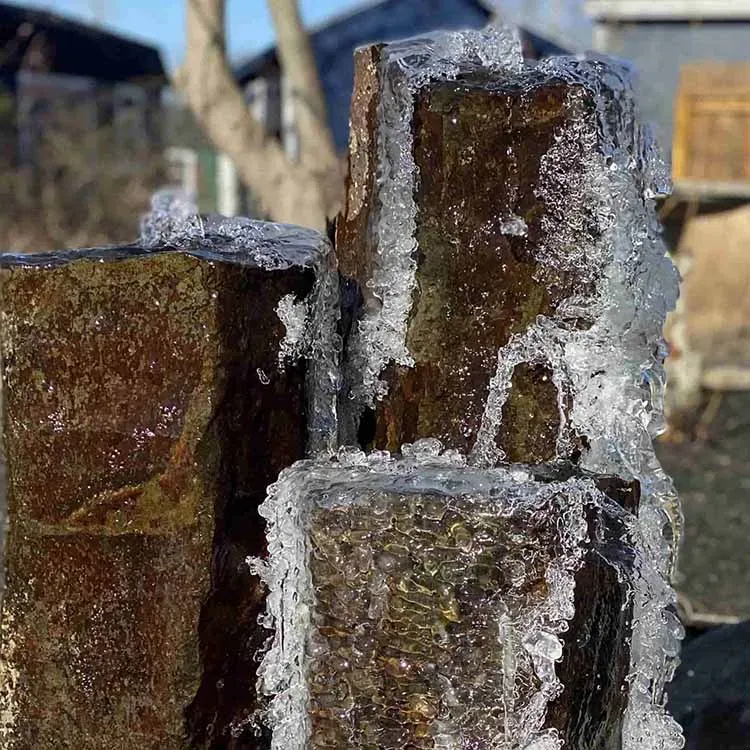 Icy water trickling down dark, stacked stone cylinders in an outdoor setting.