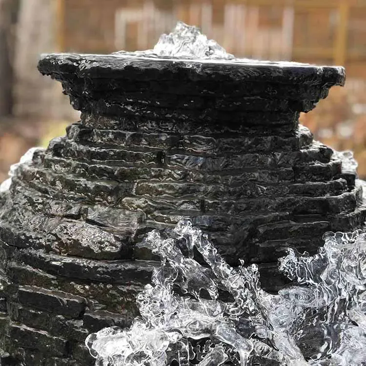 Water fountain with tiers of dark, textured stone; water flows down and out.