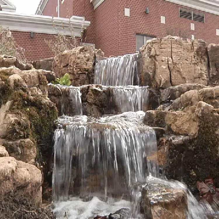 Cascading waterfall feature with tiered rock formations against a brick building.