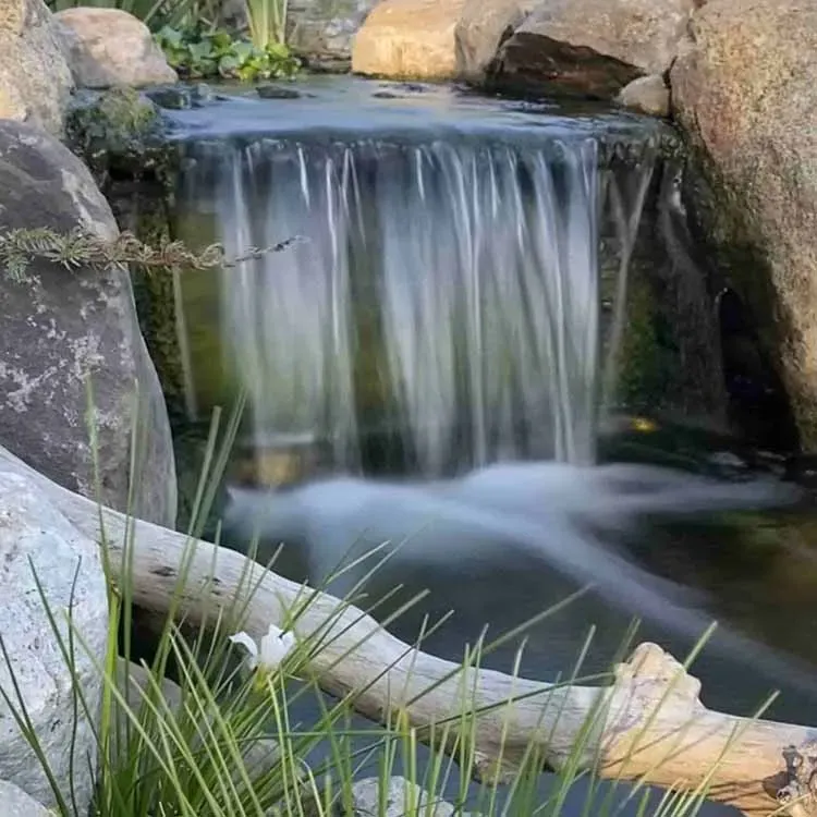 Small waterfall cascading into a pond, framed by rocks and greenery.