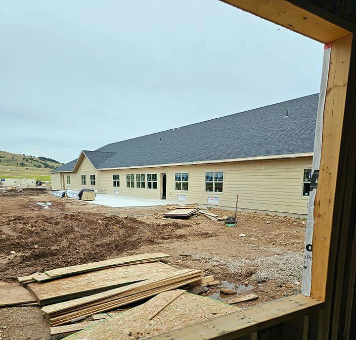 A large house is being built in the middle of a dirt field.