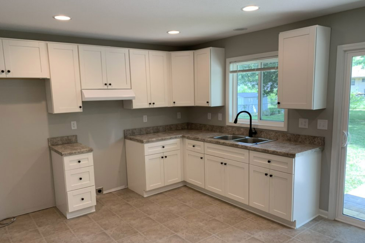 An empty kitchen with white cabinets and granite counter tops.