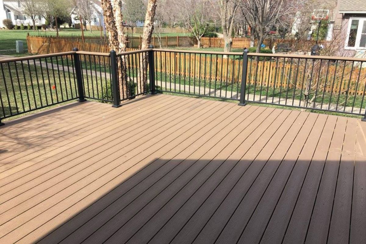 A large wooden deck with a metal railing and trees in the background.