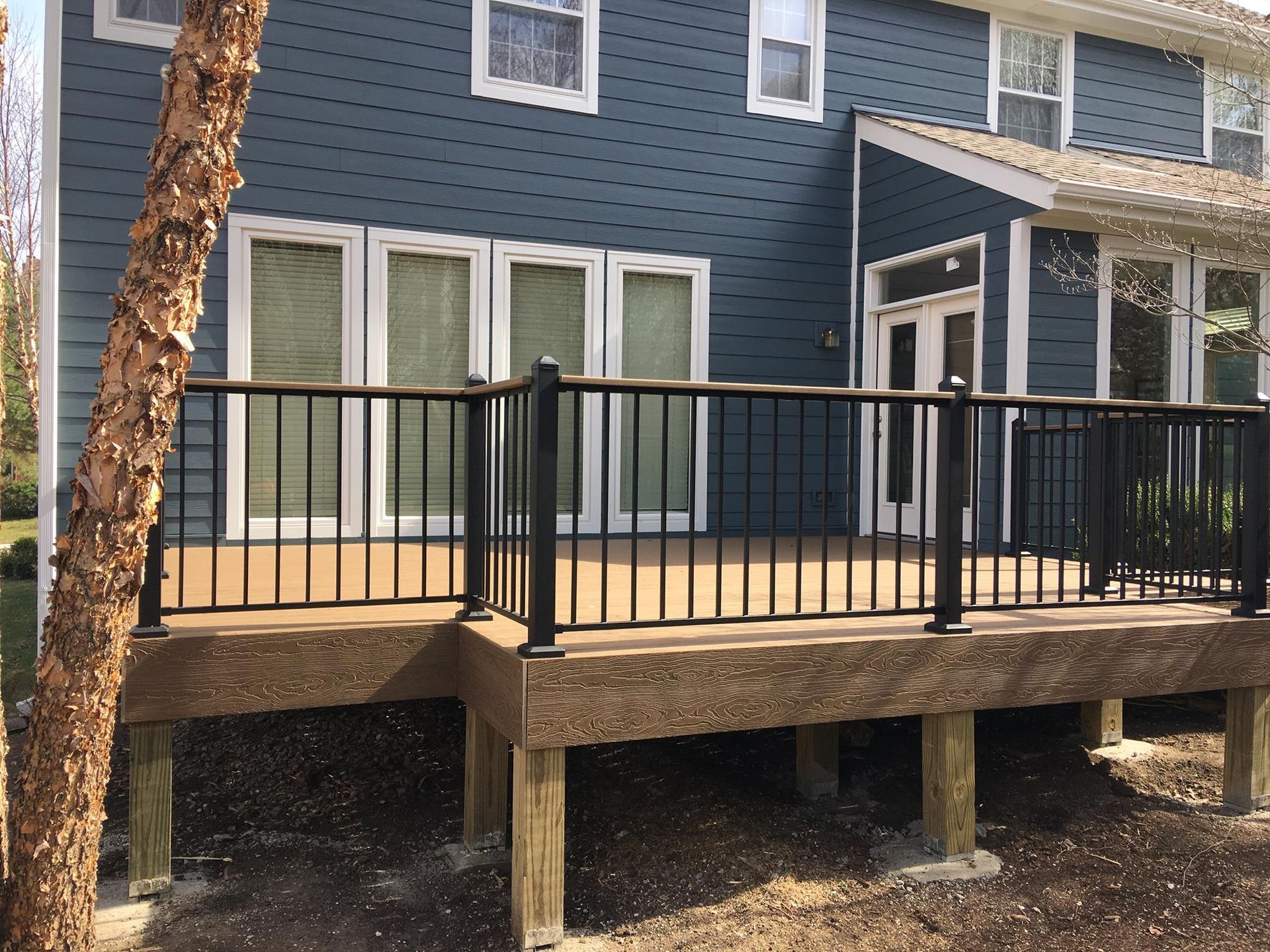 A large deck with a black railing is in front of a blue house.