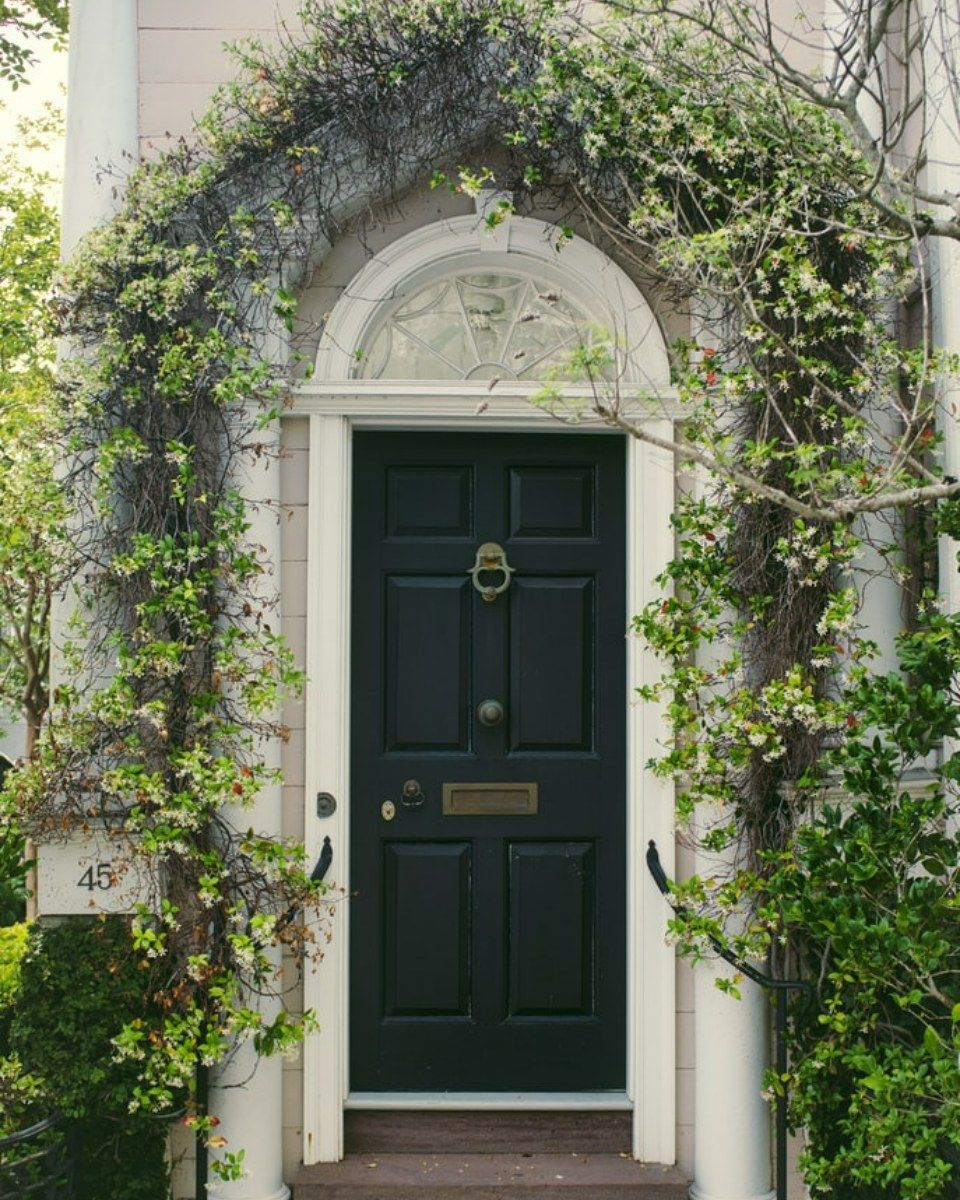 A black door with a white arch and ivy growing around it