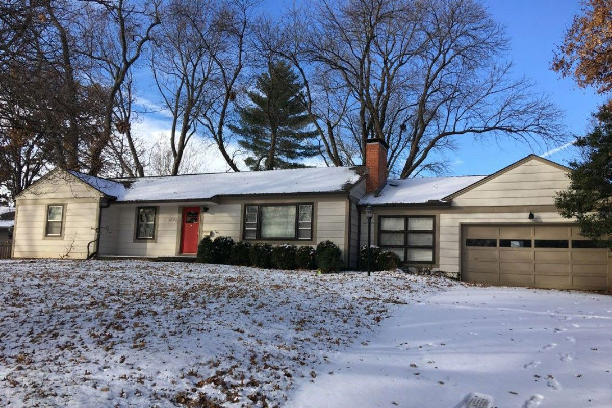 A house with a garage and a red door is covered in snow