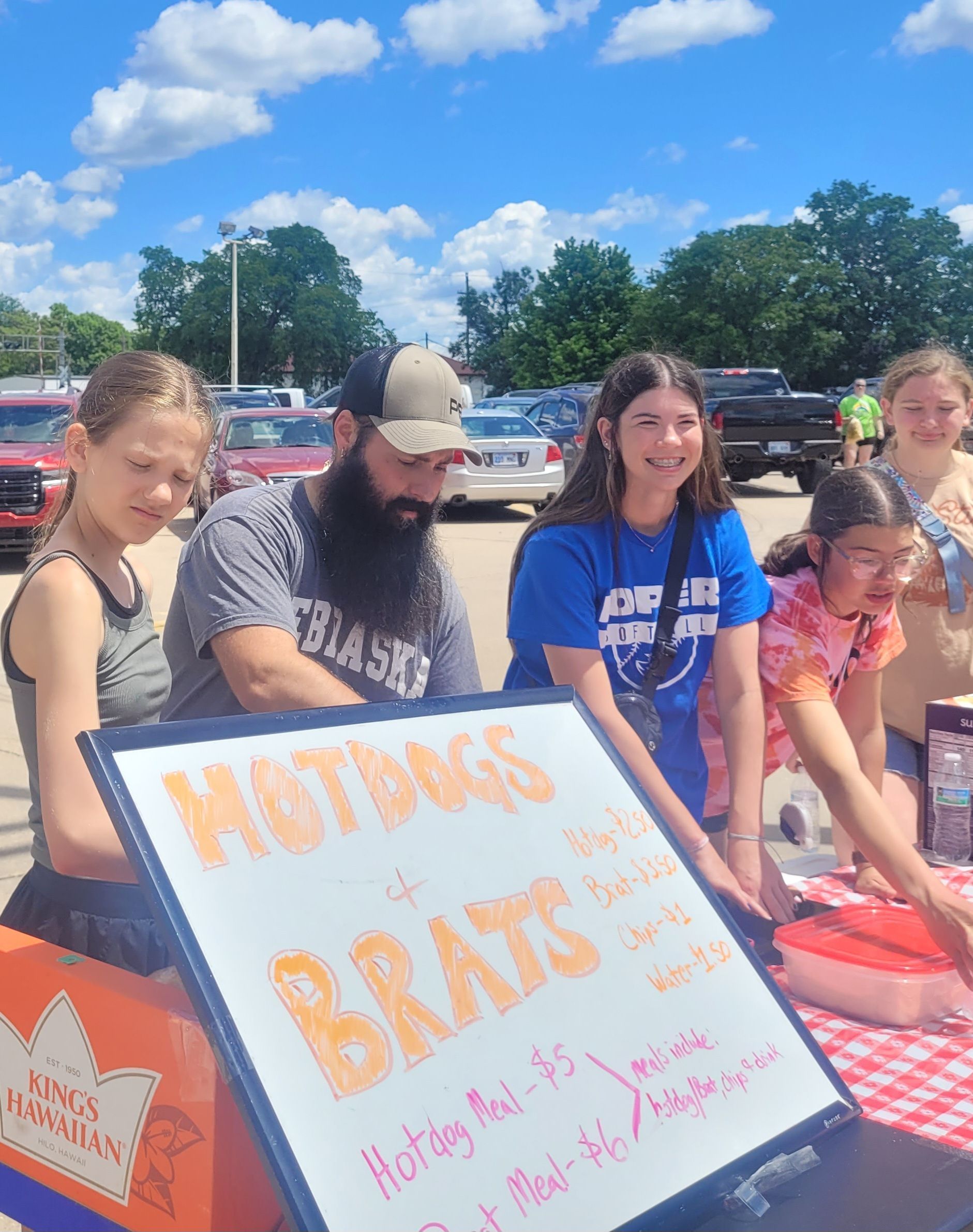 A group of people are sitting around a table holding a sign that says hotdogs and brats