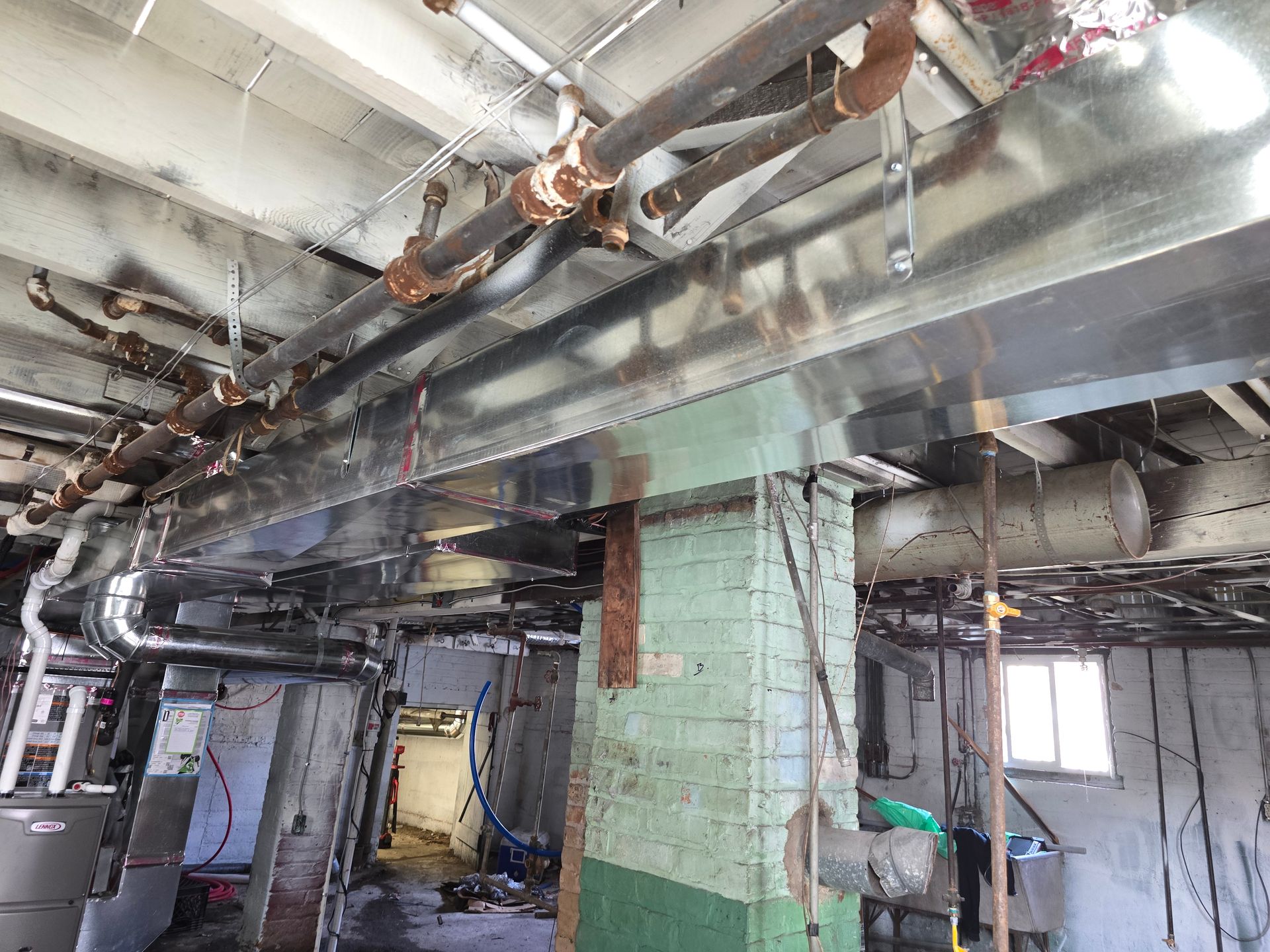 Damaged interior with exposed pipes, torn ceiling, and debris in a building under renovation