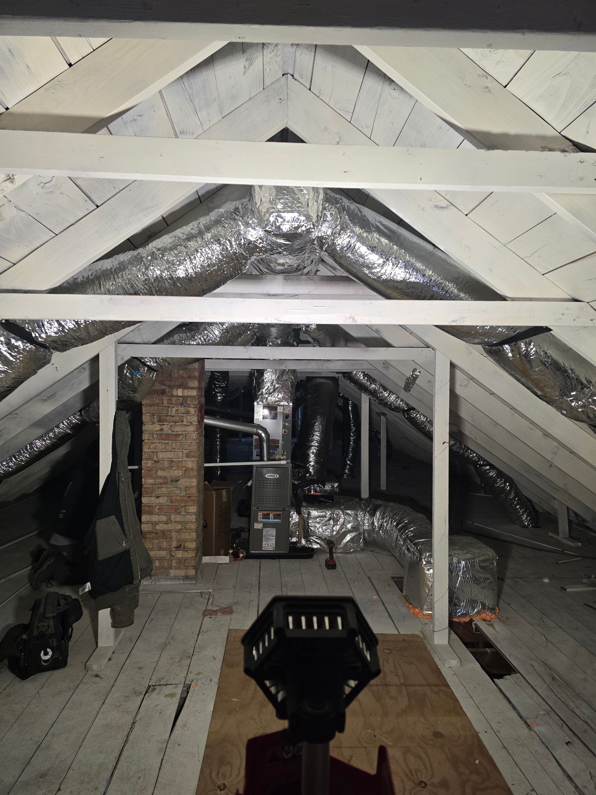 Attic interior with white beams, foil insulation, wooden floor, and a flashlight in the foreground
