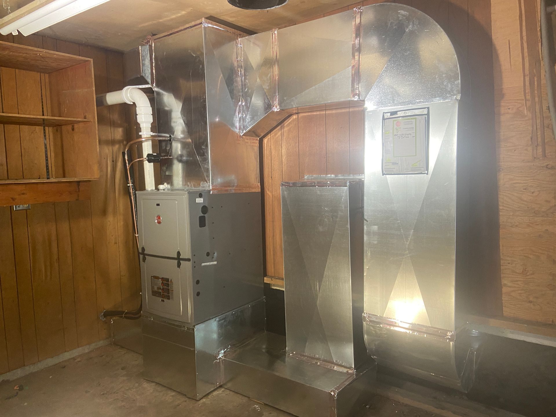 Metal HVAC ducts and a furnace unit inside a small wooden utility room.