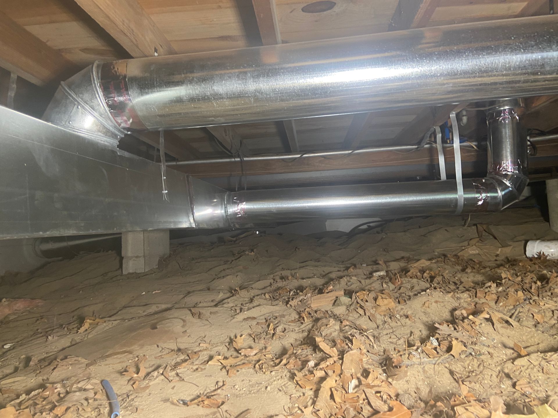 Crawlspace with insulated metal ductwork under exposed wooden floor joists and dirt ground
