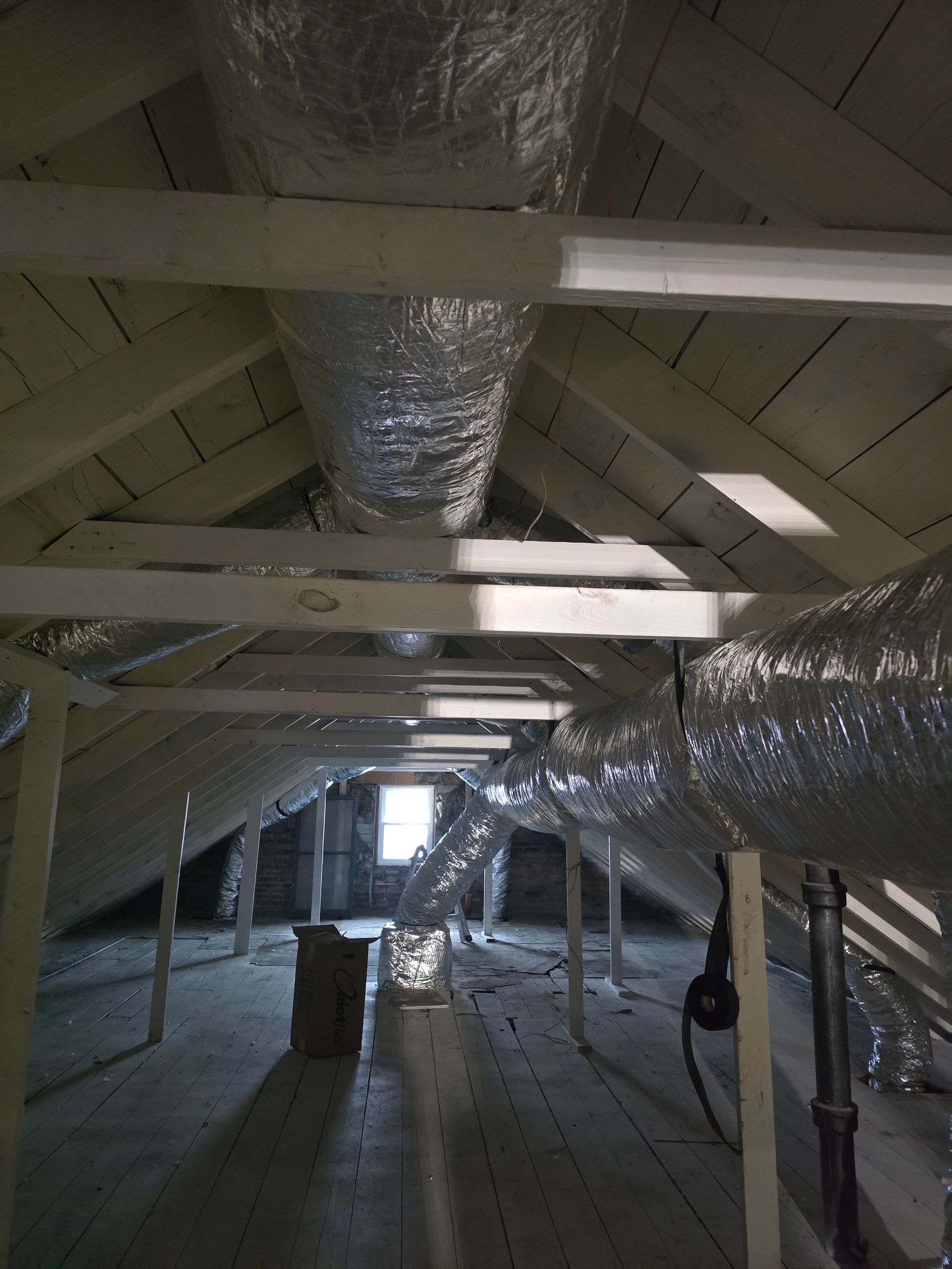 Attic with exposed beams, insulation, and ductwork in a dimly lit unfinished space