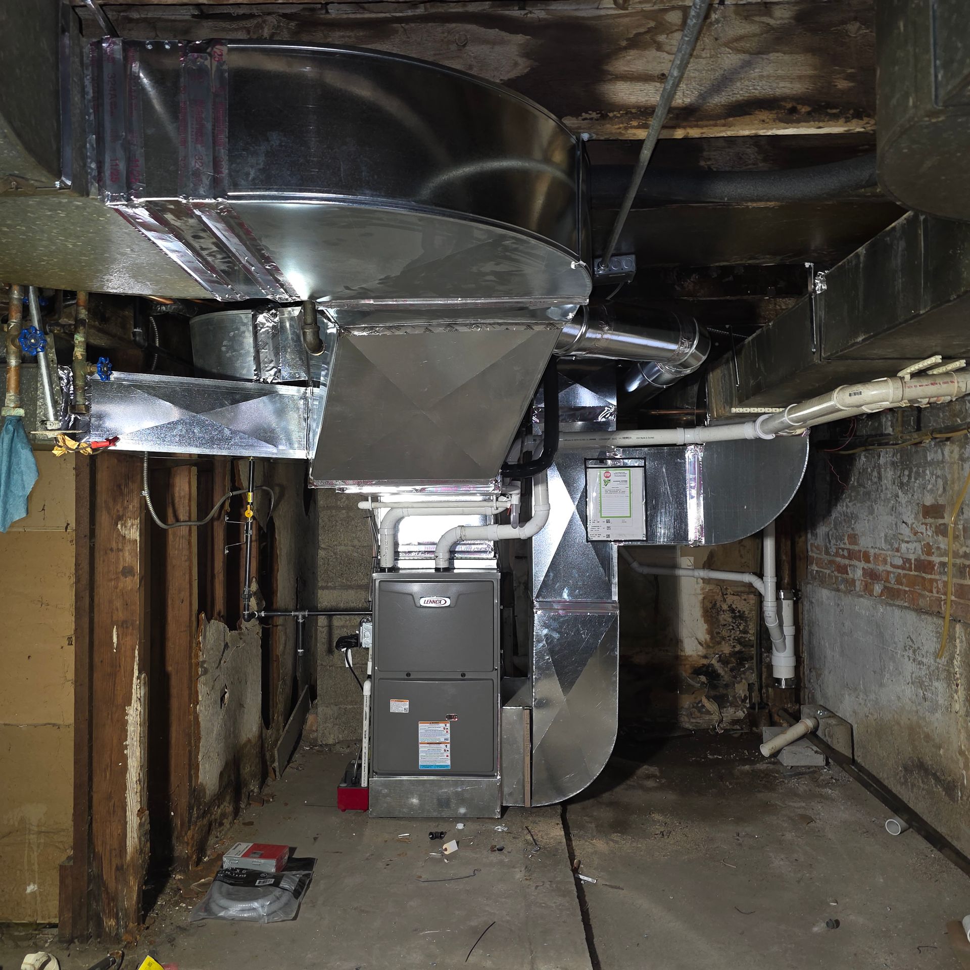 Basement with large silver HVAC ductwork and furnace unit in a narrow unfinished space