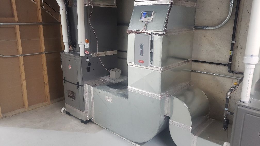 A residential HVAC furnace unit with metal ductwork, pipes, and a digital thermostat mounted in a basement.