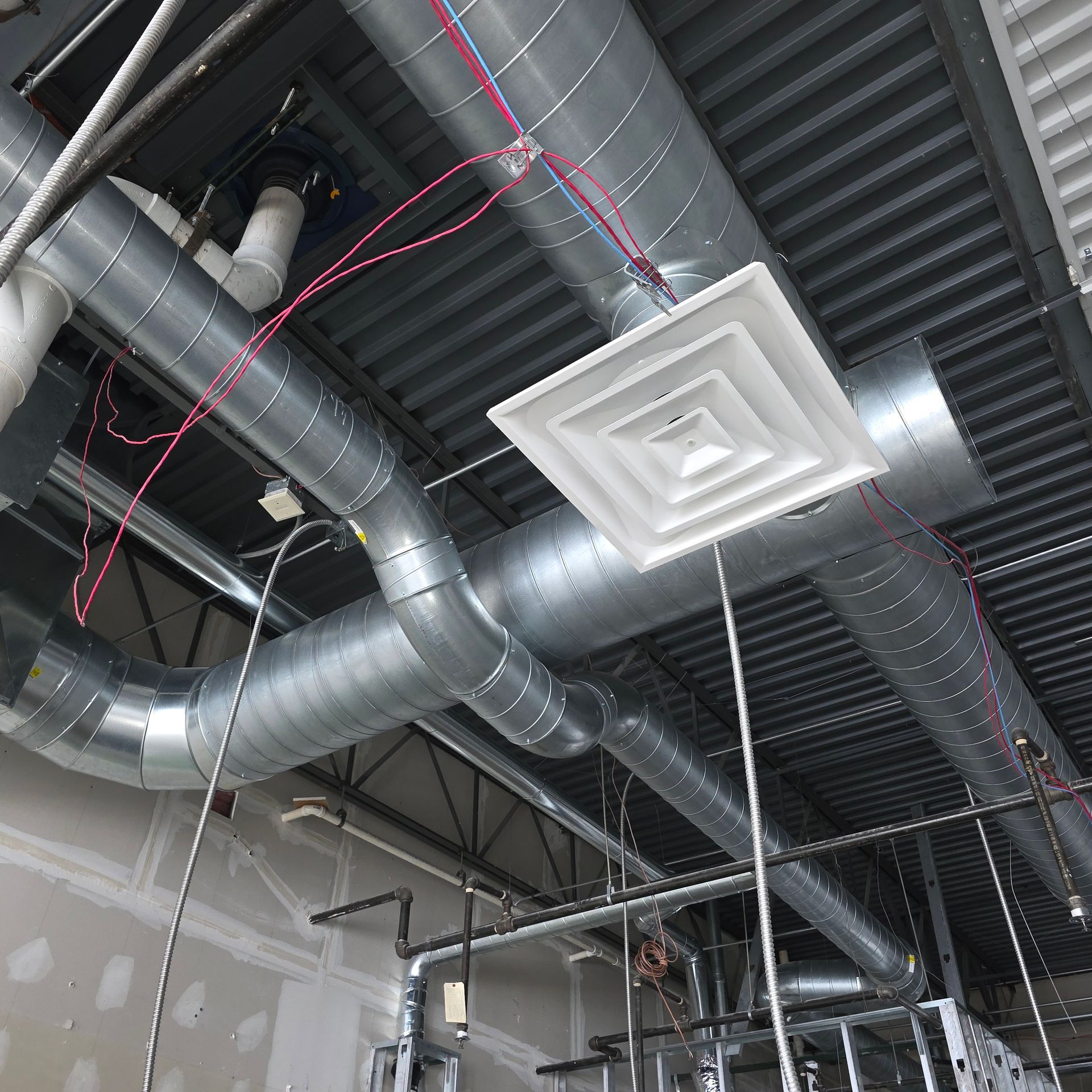 Ceiling ductwork and vents in an industrial interior with exposed pipes and metal roof