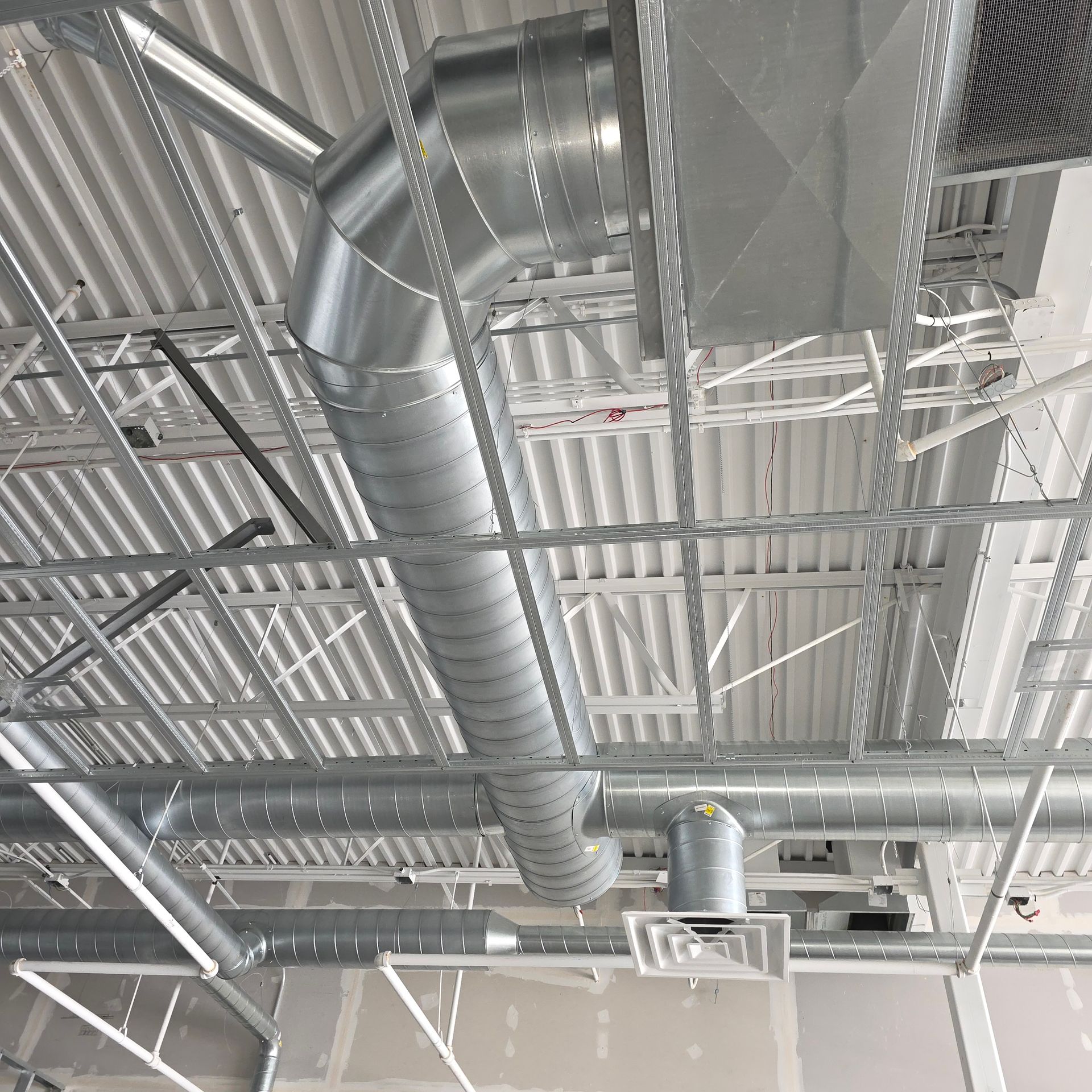 Industrial ceiling with exposed silver ductwork, pipes, and fluorescent lights in a warehouse-like interior