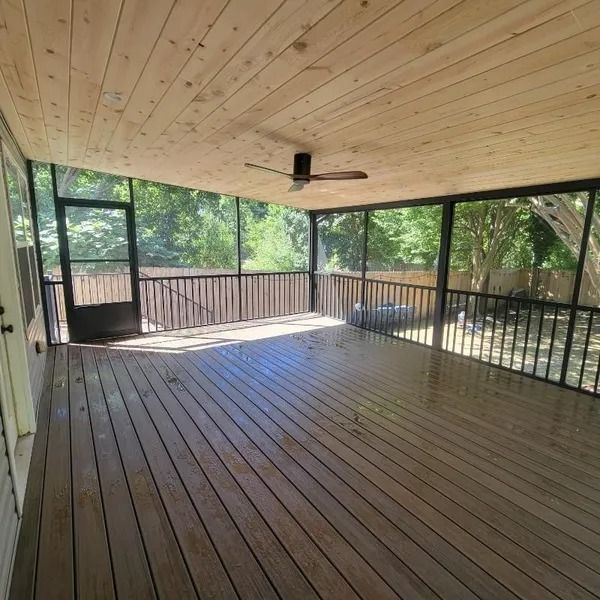 An empty screened in porch with a ceiling fan