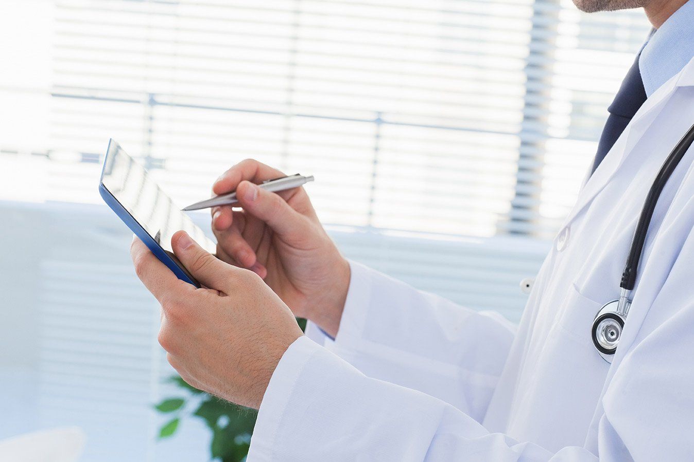 Doctor in white coat writing on tablet, stethoscope, indoors.