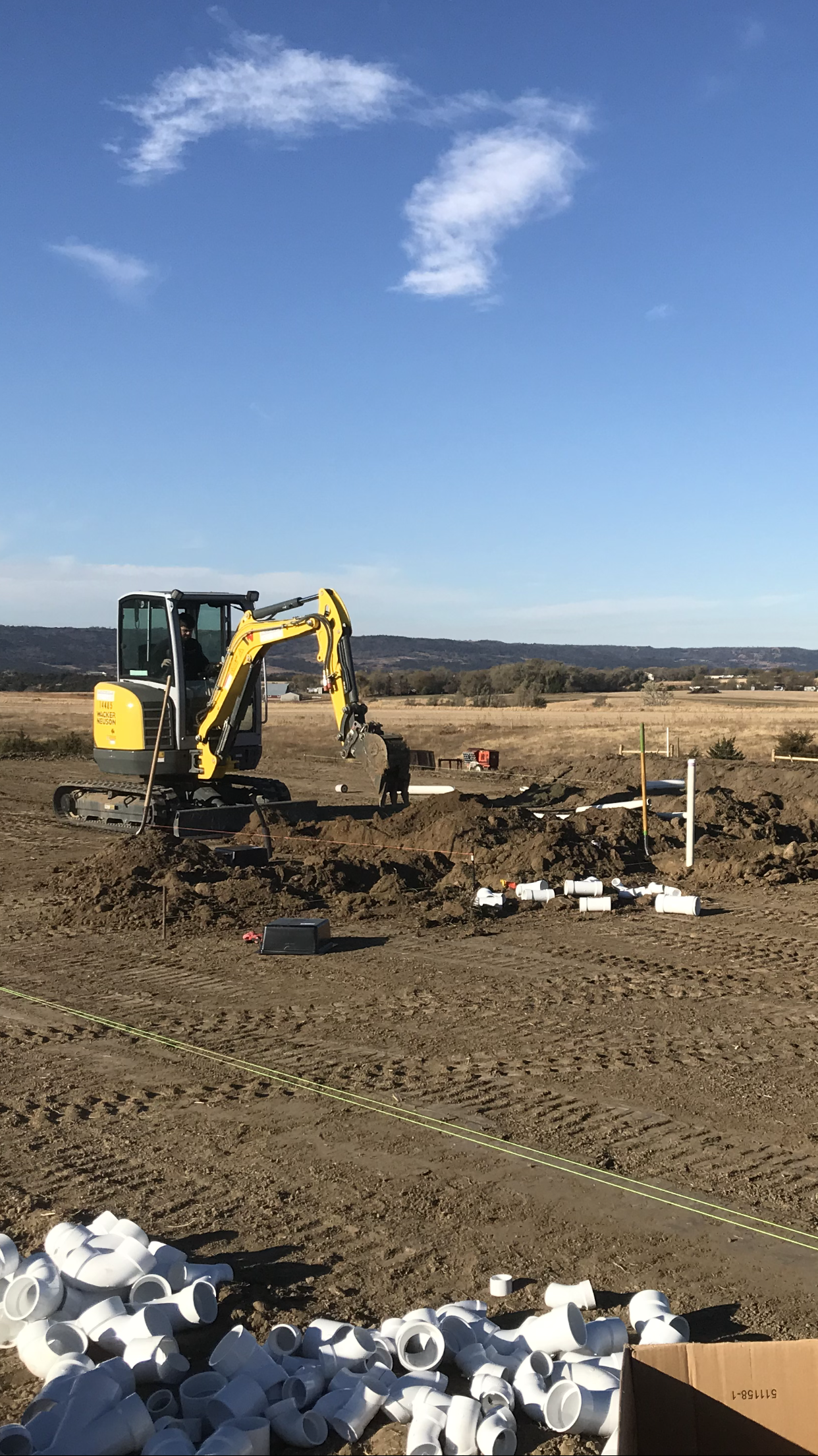 A yellow excavator is digging a hole in a dirt field.