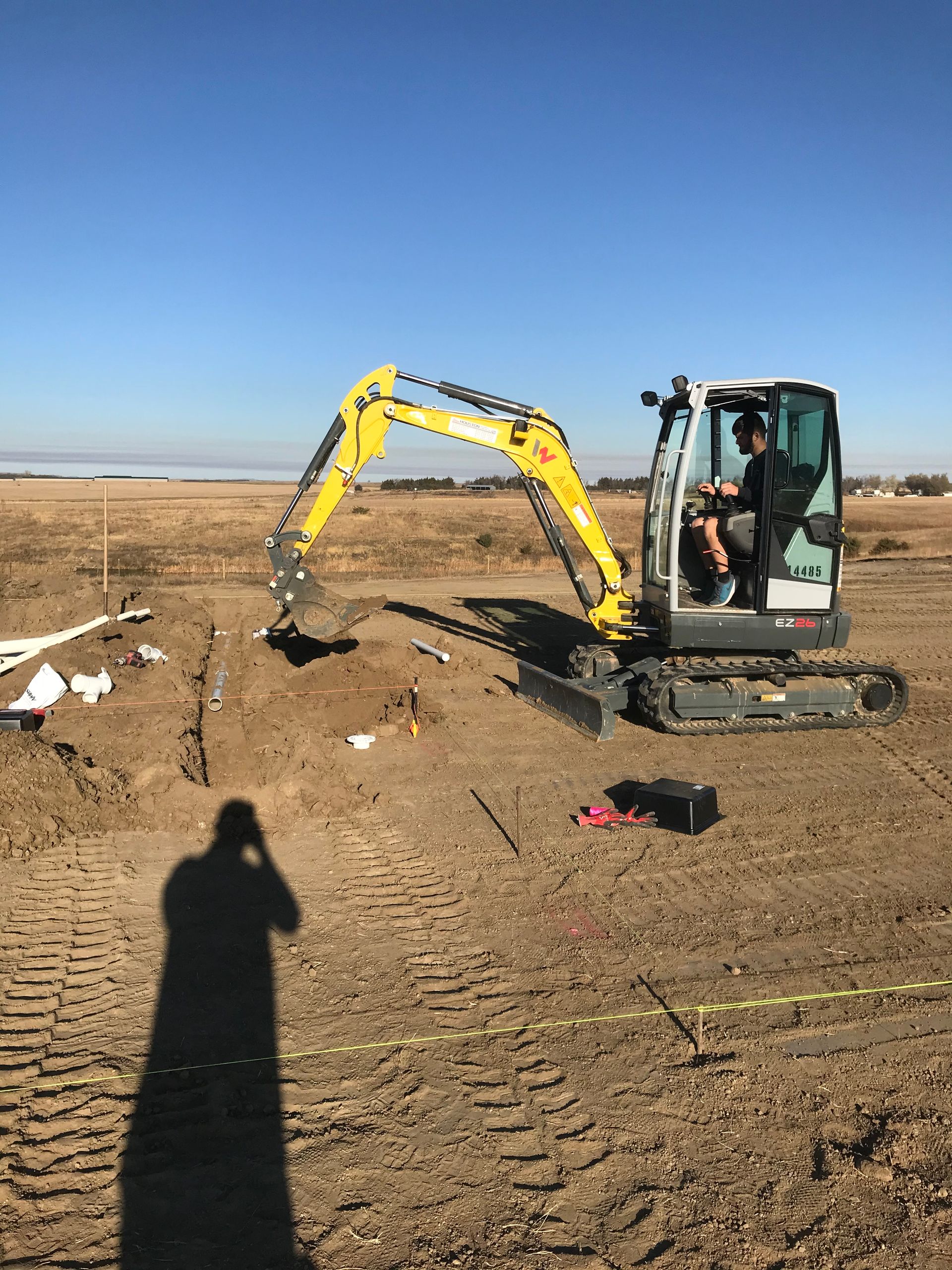 A man is driving a yellow excavator in a dirt field.