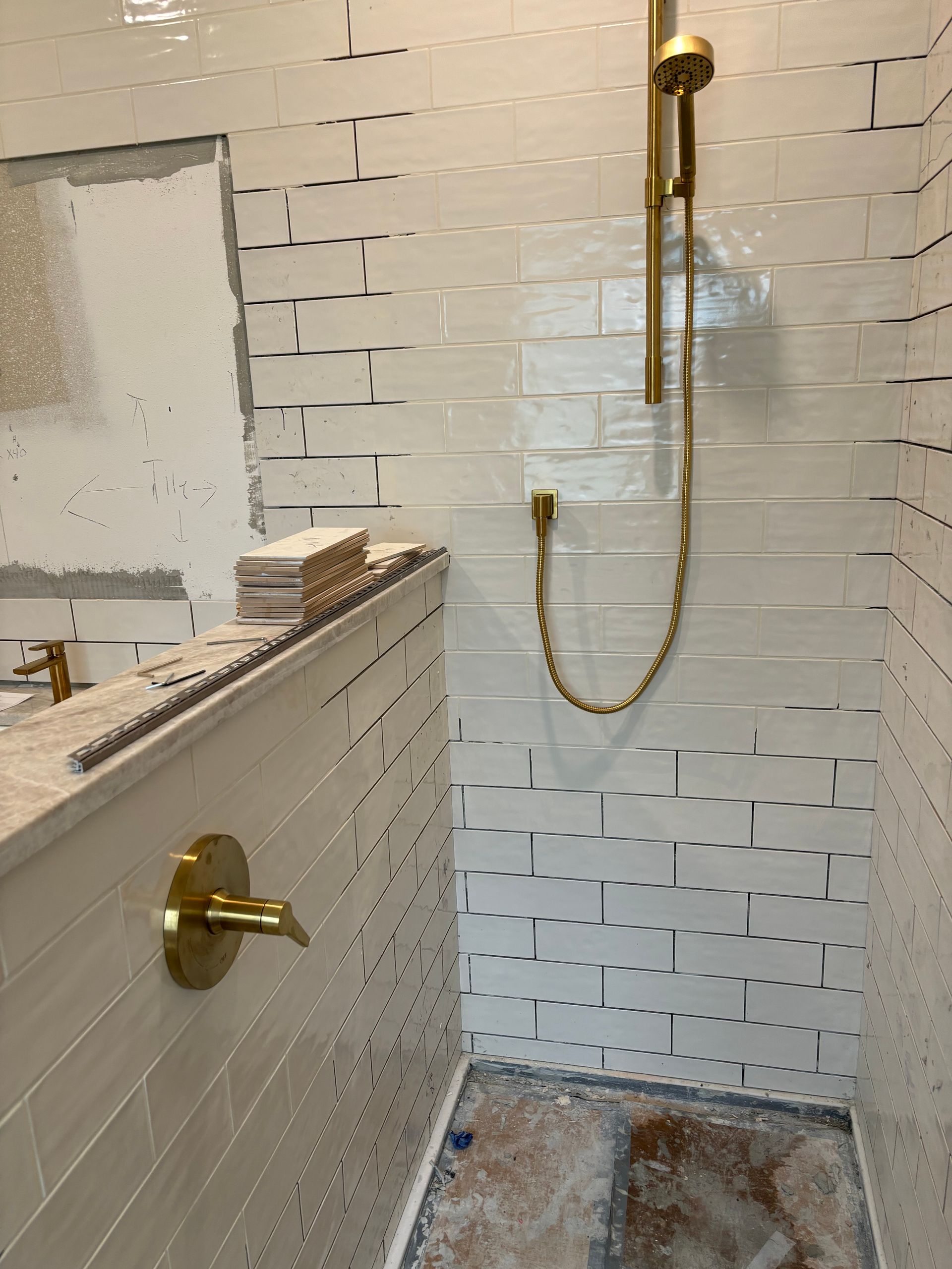 A bathroom with white tiles and a gold shower head