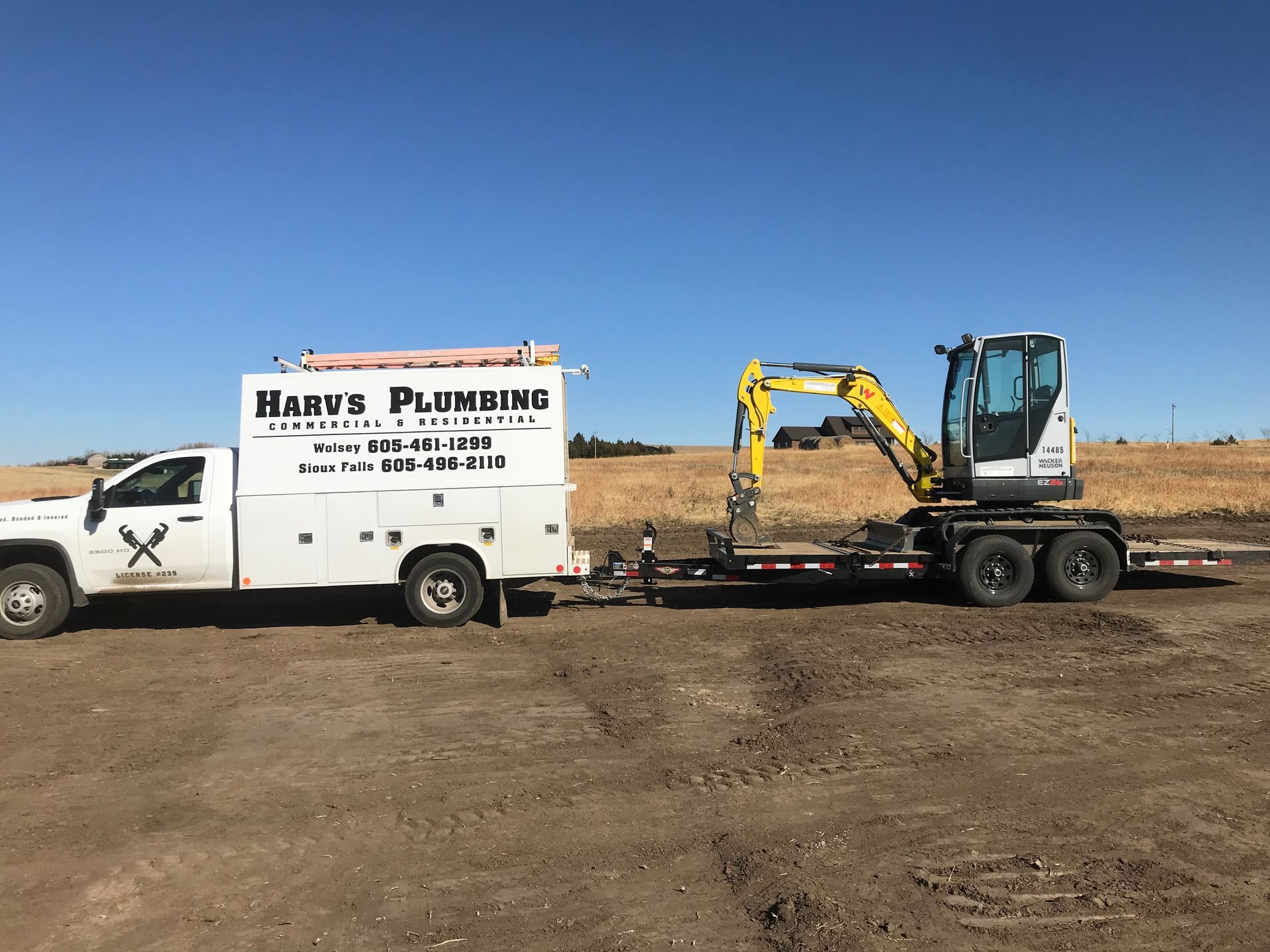 A plumbing truck is towing a small excavator on a trailer.