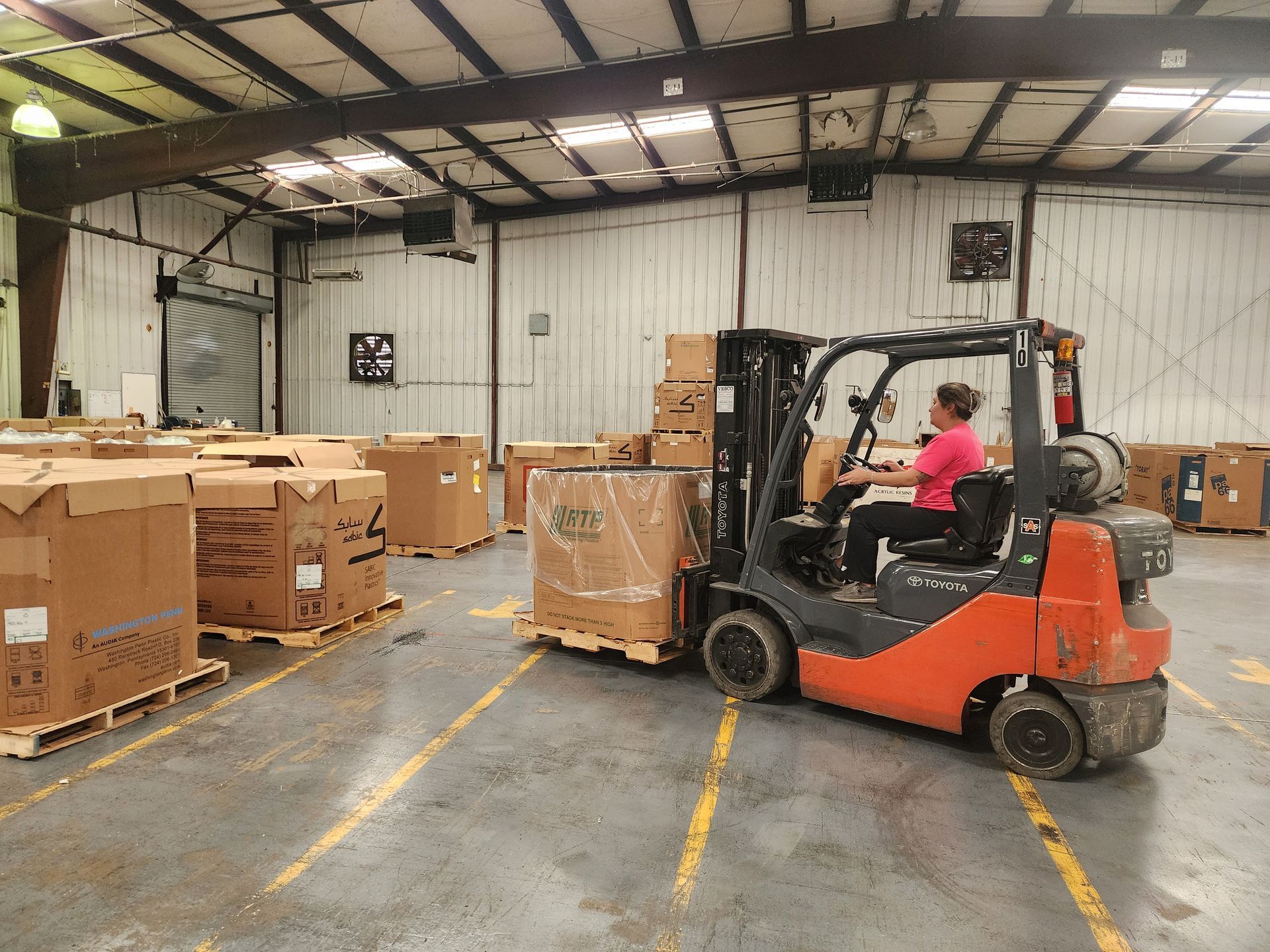 A woman is driving a forklift in a warehouse filled with boxes.