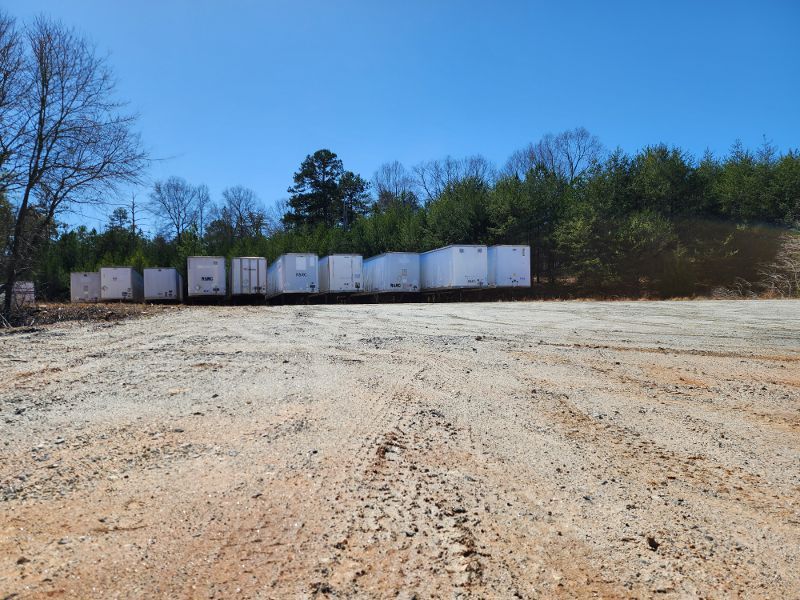 A train is going through a dirt field with trees in the background