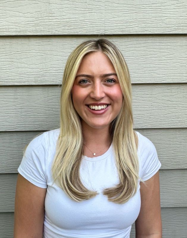 A blonde woman is wearing a white shirt and smiling for the camera.