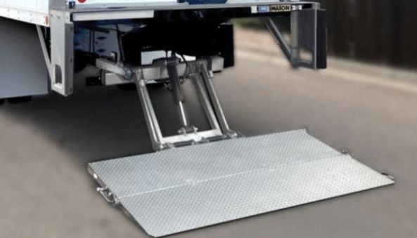 Truck with a hydraulic liftgate extended onto asphalt, ready for loading/unloading cargo.