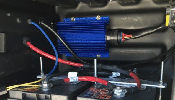 Blue electrical converter wired to two black batteries, mounted inside a dark enclosure.