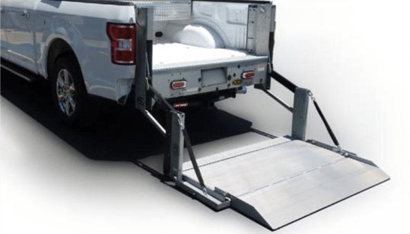 A truck bed with an attached wheelchair lift extended to the ground; metal ramp.