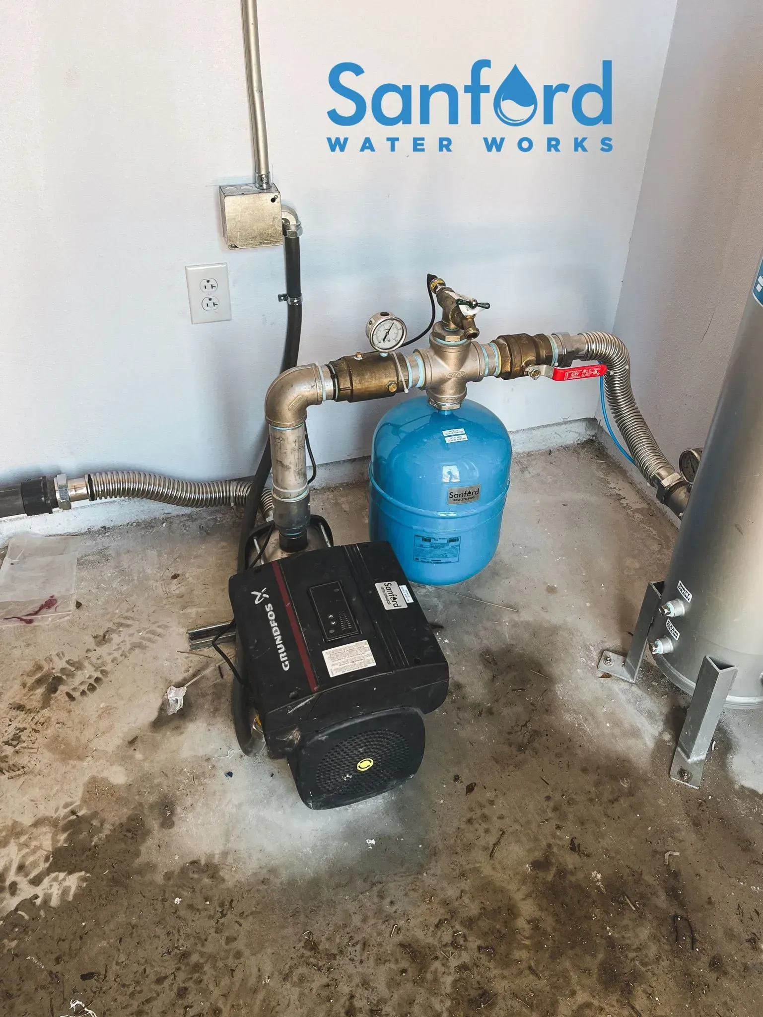 Water pump system in a concrete utility room. The system has a blue pressure tank and several pipes. 