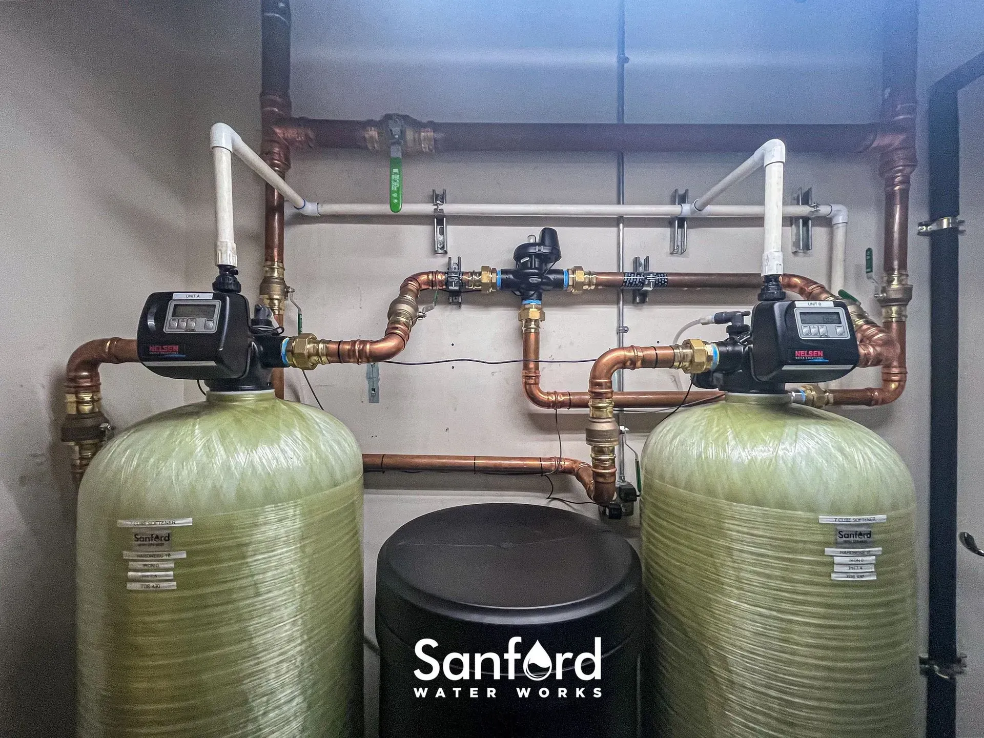 Two water softener tanks with copper piping, a black tank, and Sanford Water Works logo.