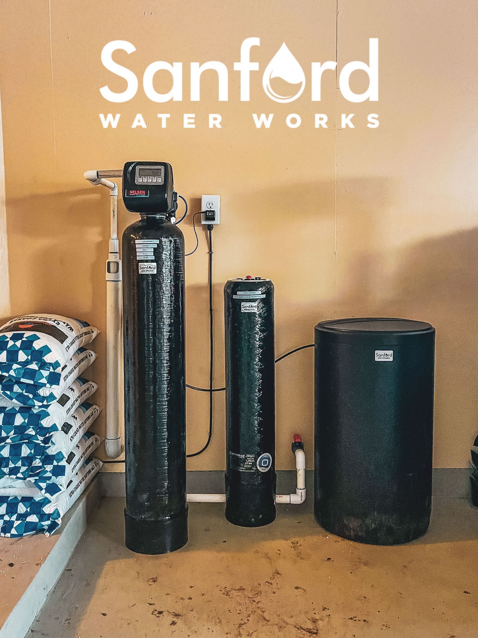 Water softening system with three black tanks and bags of salt in a utility room.