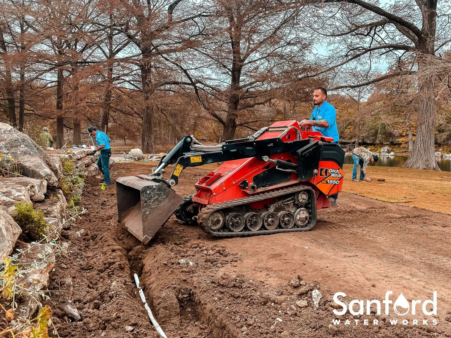 Construction crew operating a mini excavator digging a trench outdoors.