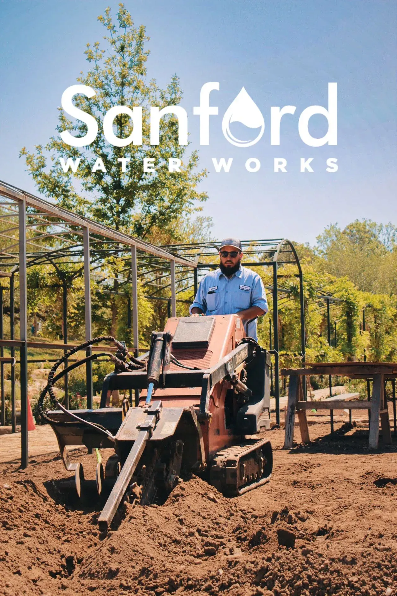 Man operating a small excavator in a dirt area with the Sanford Water Works logo in the background.